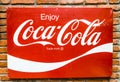 Classic trademark branding logo of CoCa-Cola on red metal sheet with red brick wall.